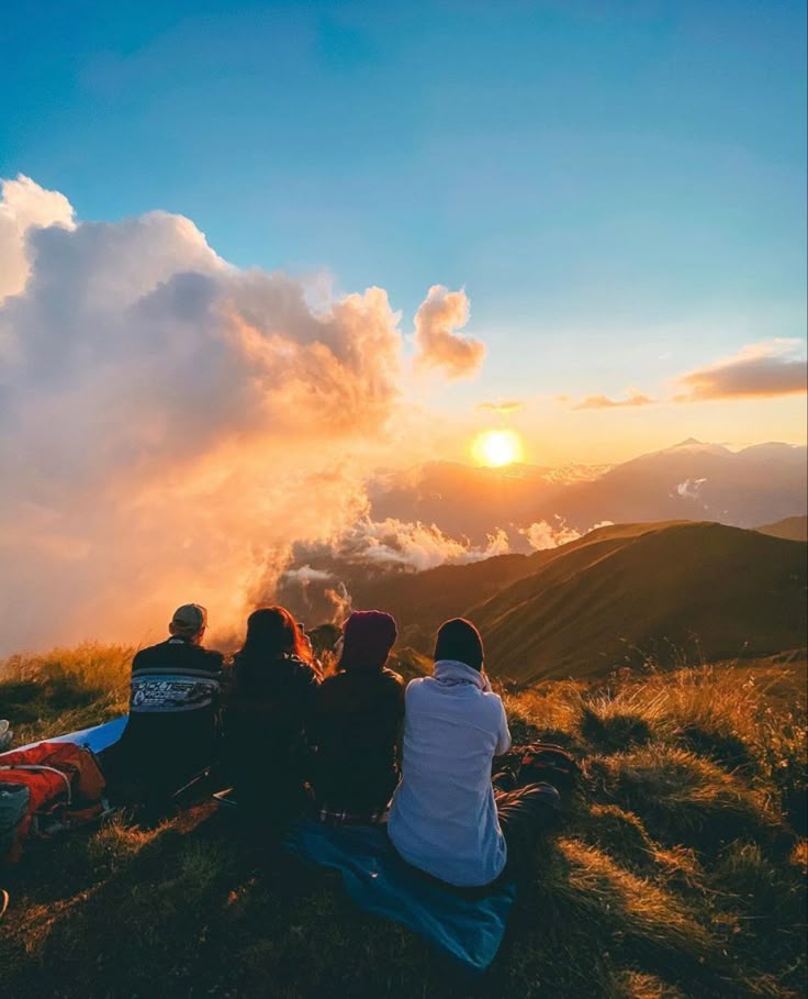 Four hikers sitting and watching the sunrise over a sea of clouds during an early morning trek.