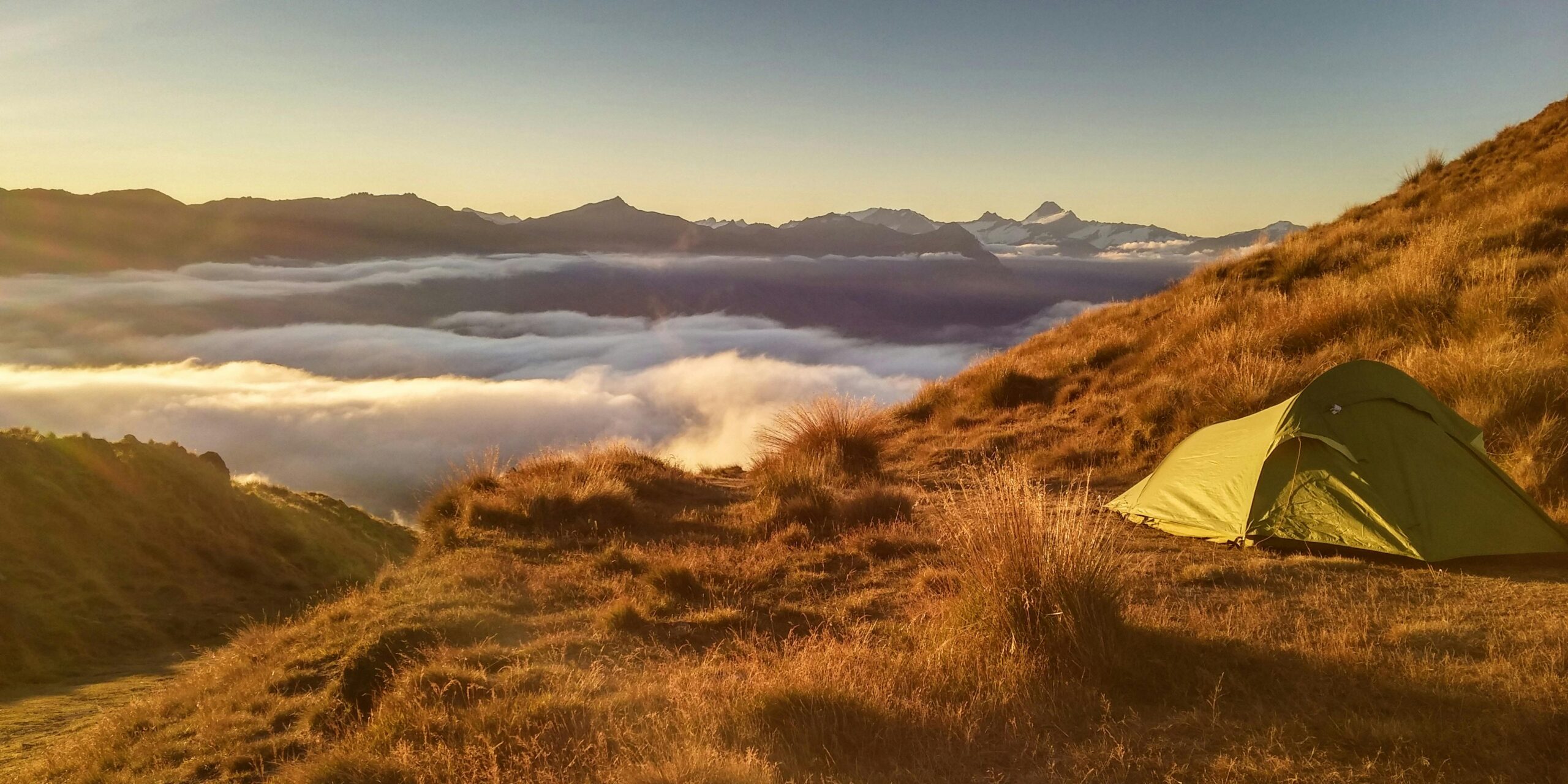 Captivating sunrise over Wanaka's mountains with a tent and sea of clouds.