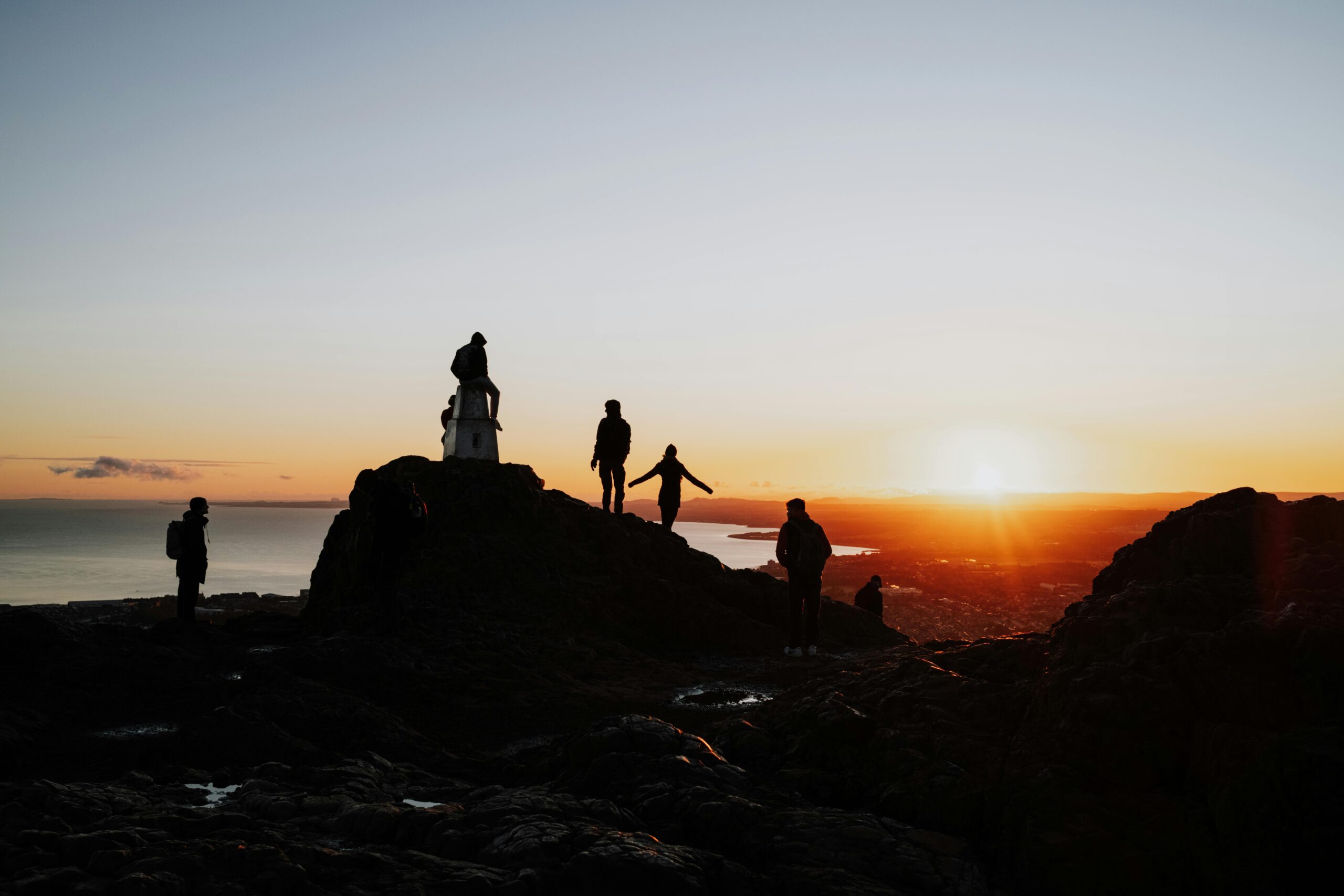 Silhouettes enjoying a stunning sunset view from Arthur's Seat in Edinburgh, Scotland.